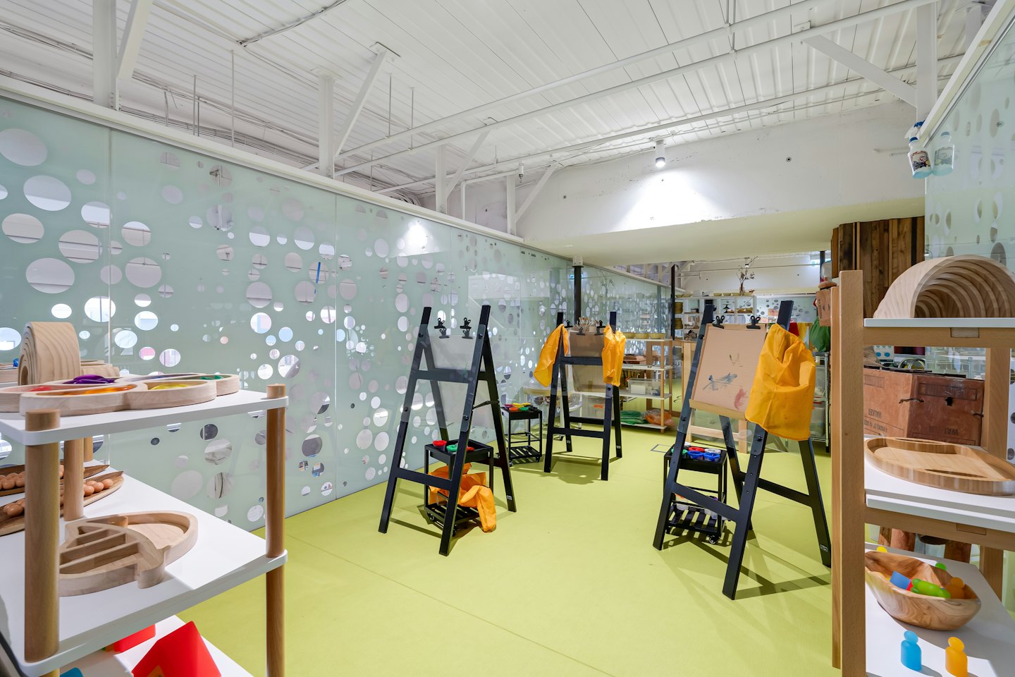 Modern classroom features wooden toys and empty art easels.